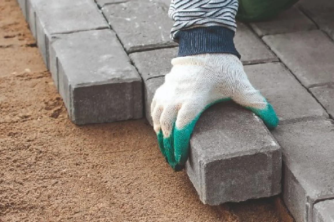 Hand in Arbeitshandschuh verlegt Pflasterstein